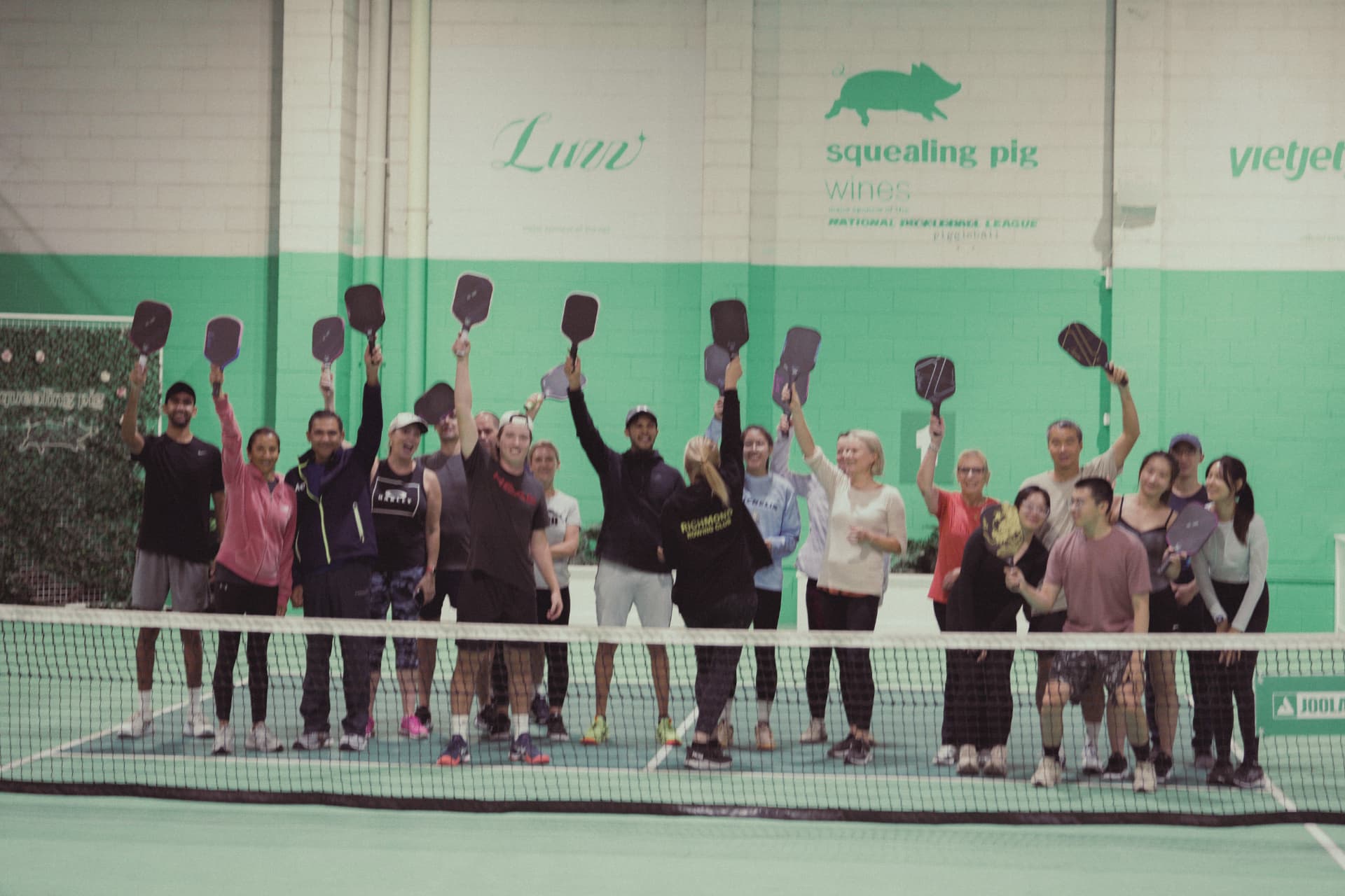Group of players raising their paddles under the Luzz court signage